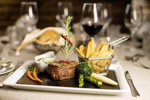 Ein angerichtetes Essen mit Steak, Pommes und Gemüse, im Hintergrund Weingläser.