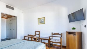 Un dormitorio con una cama, dos sillas de madera, una mesita, un televisor y un armario.