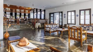 Un vestíbulo amplio con mobiliario de madera, una escalera central y ventanas grandes que dejan entrar luz natural.
