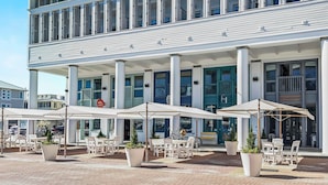 Un bâtiment à deux étages doté d’une entrée centrale, d’une terrasse avec des parasols et d’une enseigne indiquant « 25, place centrale ».