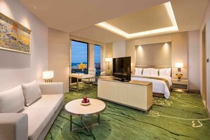 Ein Hotelzimmer mit Bett, Fernseher, Sofa, kleinem Tisch und Blick auf die Stadt.