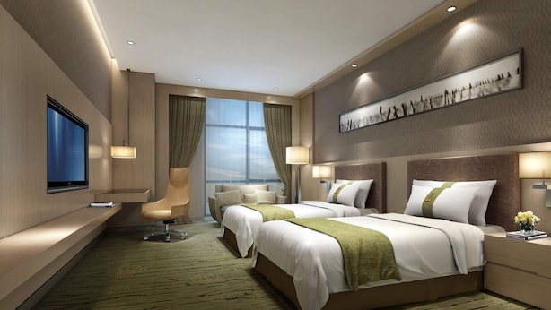 A hotel room with two beds, a desk, a chair, a TV, and a large window.