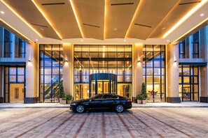 Ein moderner Hotel Eingang mit einem geparkten Auto davor, großen Glasüren und einer Treppe zum Eingang.