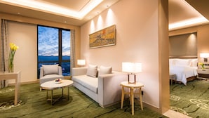 A hotel room with a large window, a sofa, a round table, and a bed.
