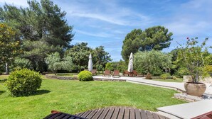 Un jardin agrémenté de bancs en bois et de parasols, entouré d’arbres et d’une pelouse bien entretenue.