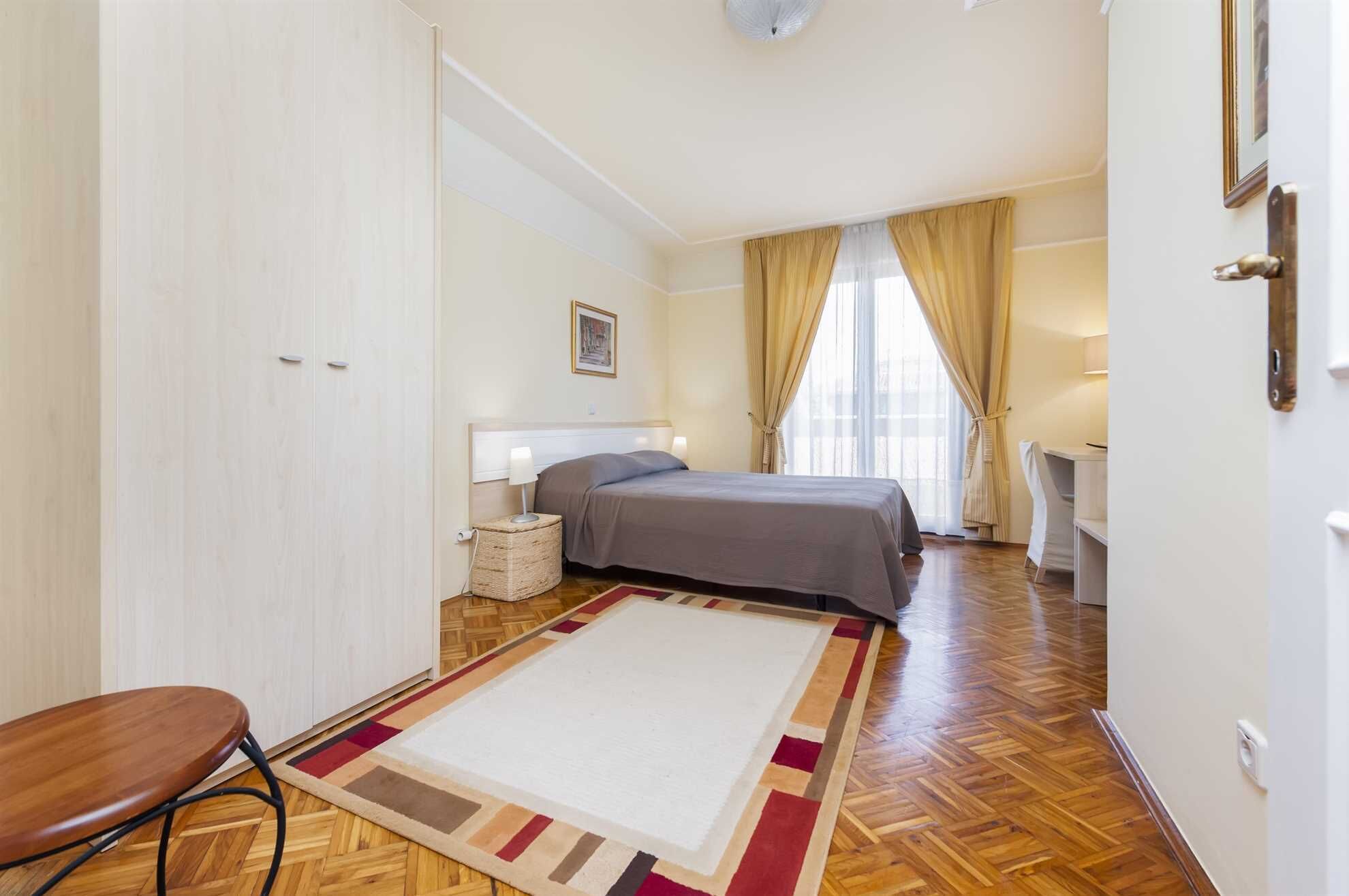 A hotel room with a bed, bedside table, lamp, and a chair.