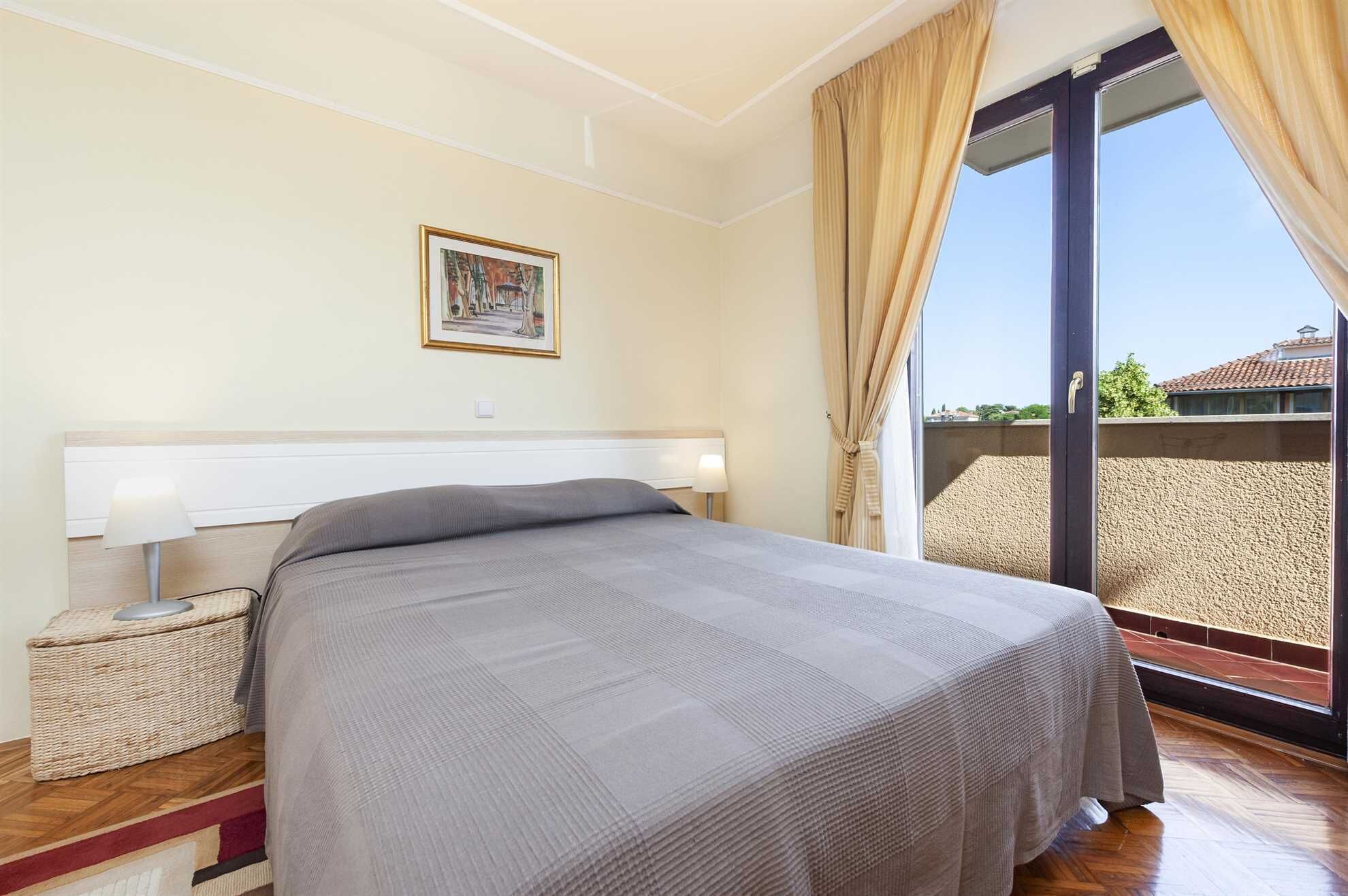 A hotel room with a bed, a bedside lamp, a framed picture on the wall, and a view of the outside balcony.