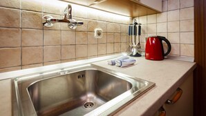 A kitchen with a stainless steel sink, a red kettle, and a towel on the counter.