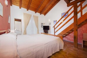 Une chambre avec un grand lit, des poutres apparentes en bois au plafond, une télévision et un escalier.