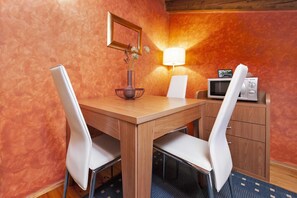 Un coin repas avec une table en bois, des chaises blanches, une lampe, un four à micro-ondes et un meuble.