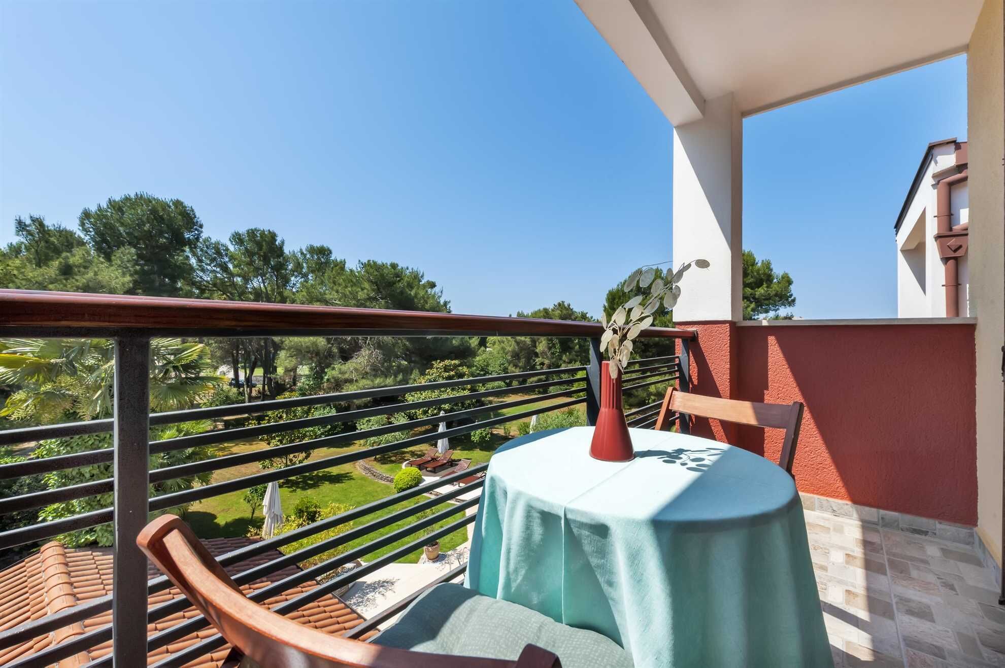 Un balcone con tavolo e sedie, affacciato su un giardino e alberi.