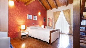 A hotel room with a wooden floor, a bed with white bedding, a nightstand with a lamp, and a window with curtains.