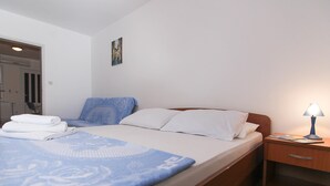 A neatly made bed with a blue blanket and white pillows, a wooden nightstand with a lamp, and a door leading to another room.