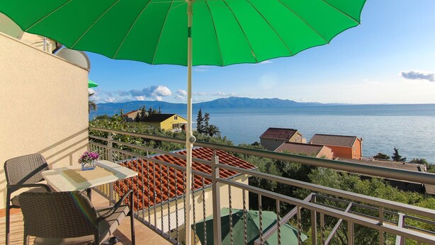 A balcony with a green umbrella, wicker chairs, a small table with flowers, and a view of the sea and mountains. - VILLA ALEX  One-Bedroom Apartment (ANA) (Podaca)