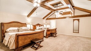Ein geräumiges Schlafzimmer mit einem großen Bett, einem kleineren Bett, einer Bank, einem Spiegel und einem Deckenventilator.