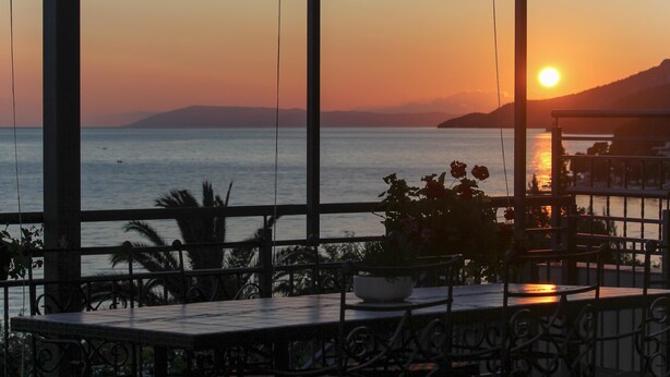 A terrace with a view of the sunset over the sea, a table with a bowl of flowers, and a railing. - VILLA ALEX Two-Bedroom Apartment (DANICA) (Podaca)