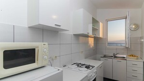 A compact kitchen with white cabinets, a microwave, a stove, and a window with a view. - VILLA ALEX Two-Bedroom Apartment (DANICA) (Podaca)
