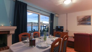 A dining area with a table set for two, a fireplace, and a view of the sea. - VILLA ALEX Two-Bedroom Apartment (DANICA) (Podaca)