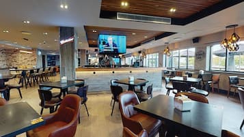 Um restaurante moderno com teto de madeira, janelas amplas e uma tela de televisão exibindo um noticiário.