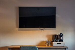 A flat-screen TV mounted on a wall, a coffee maker, and a small table with a chair. - Village Hotel Nottingham (Nottingham)
