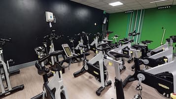 Una palestra con diverse cyclette e macchinari cardio, un muro verde e un soffitto bianco.