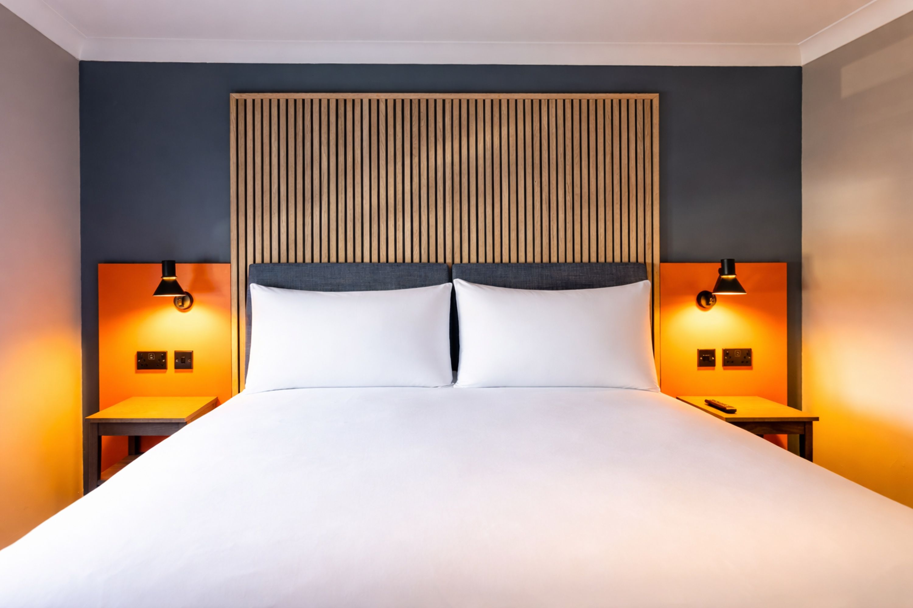 Une chambre d’hôtel moderne avec un grand lit, deux tables de chevet et une tête de lit en bois.