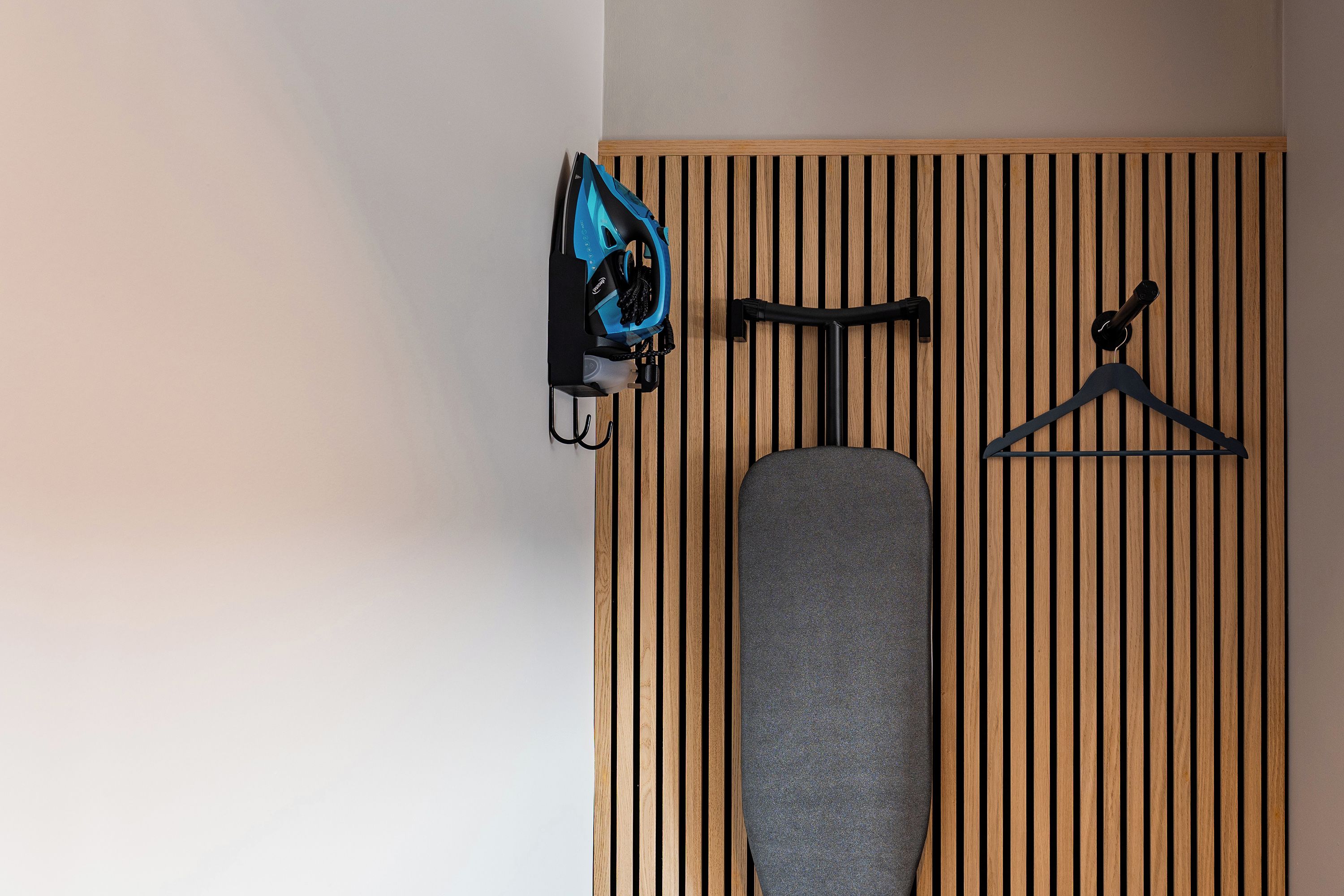 A room with a wooden slat wall, a hanging iron, and a black hanger.
