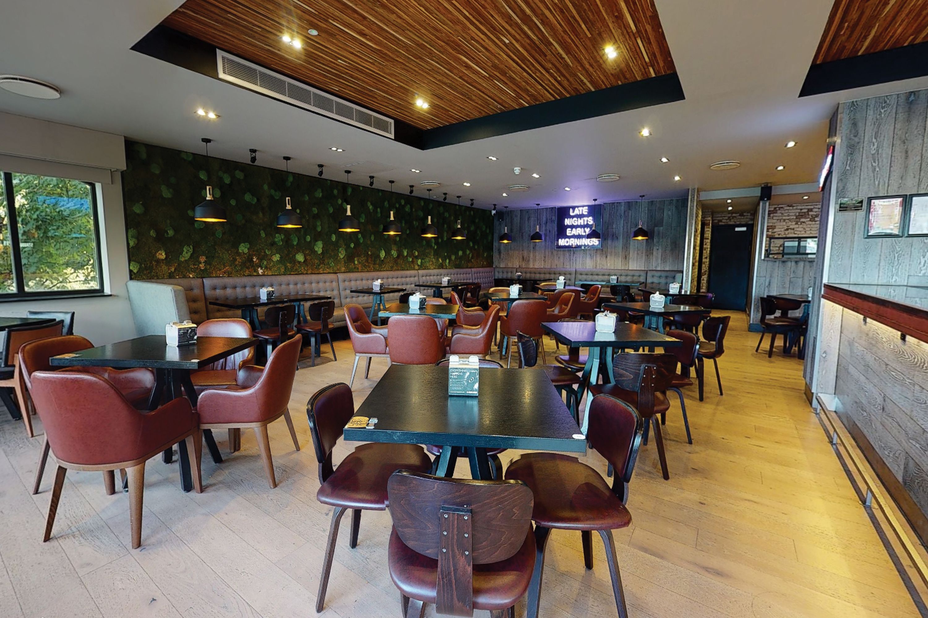 Un restaurant spacieux, doté de nombreuses tables et chaises, d’un plafond en bois et d’un mur orné d’un motif végétal.