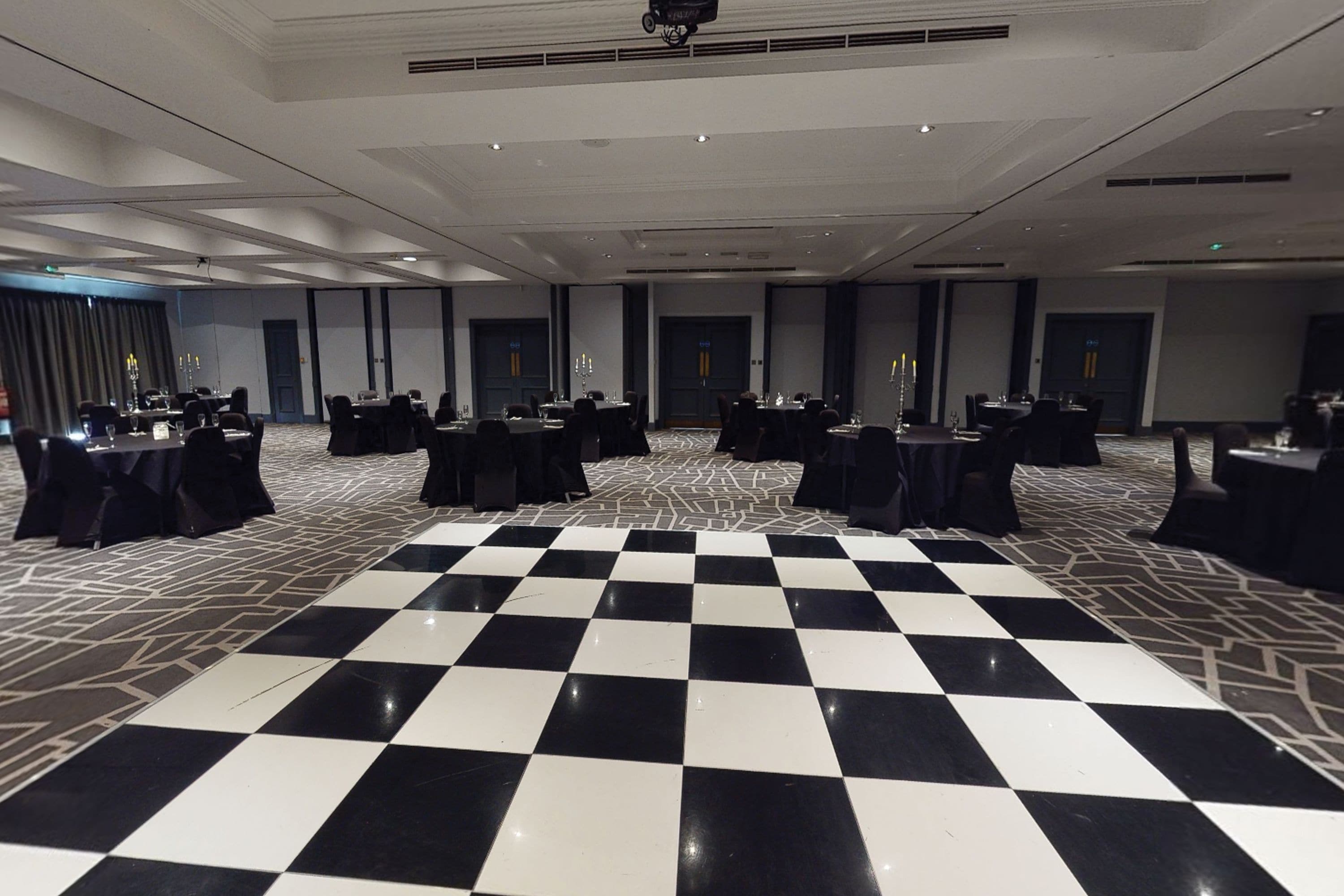 Um salão amplo com piso xadrez, várias mesas com cadeiras e um palco.