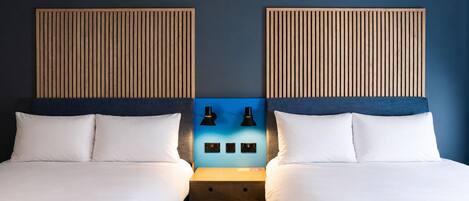 A double room with two beds, a nightstand, two wall-mounted lamps, and a blue accent wall.