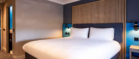 A hotel room with a large bed, a wooden headboard, two bedside lamps, and a small nightstand.