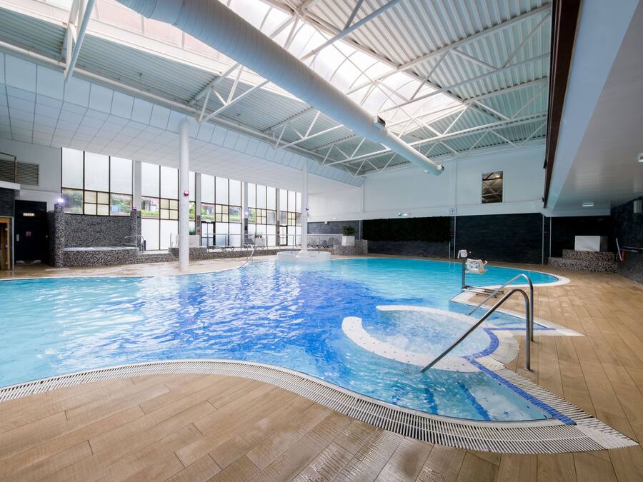 An indoor swimming pool with a tiled floor, a diving board, and a large windowed wall.