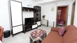 Una sala de estar con un sofá, un televisor, un armario y una mesita.
