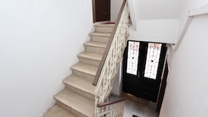 Una escalera con peldaños color beige y barandillas blancas que conduce a una puerta negra con paneles de vidrio decorativos.