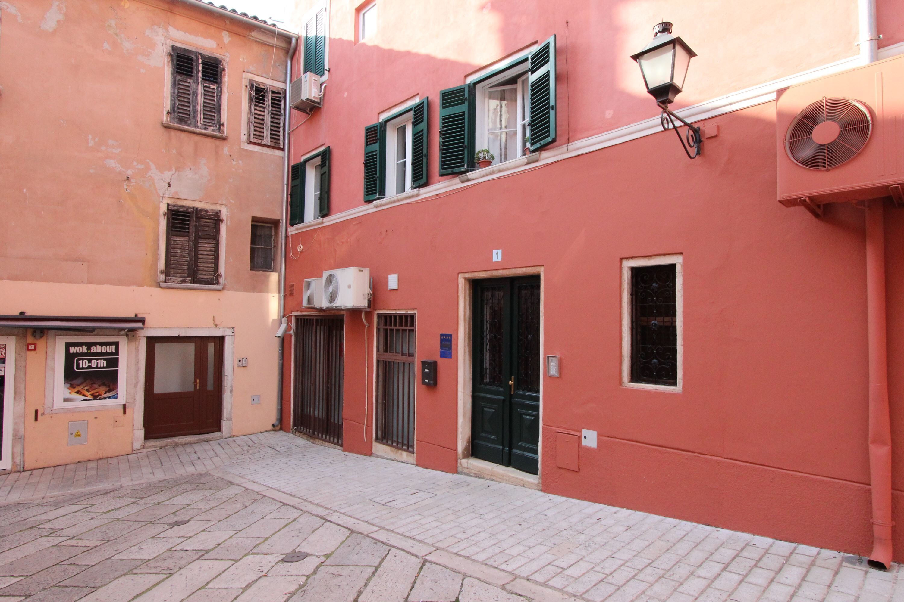 Une rue étroite bordée d’immeubles dotés de balcons, d’une porte et d’une enseigne.
