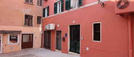 Une rue étroite bordée d’immeubles dotés de balcons, d’une porte et d’une enseigne.