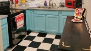 Una cocina con armarios azul claro, piso a cuadros blanco y negro, microondas rojo y un cartel que dice 'HOME'.
