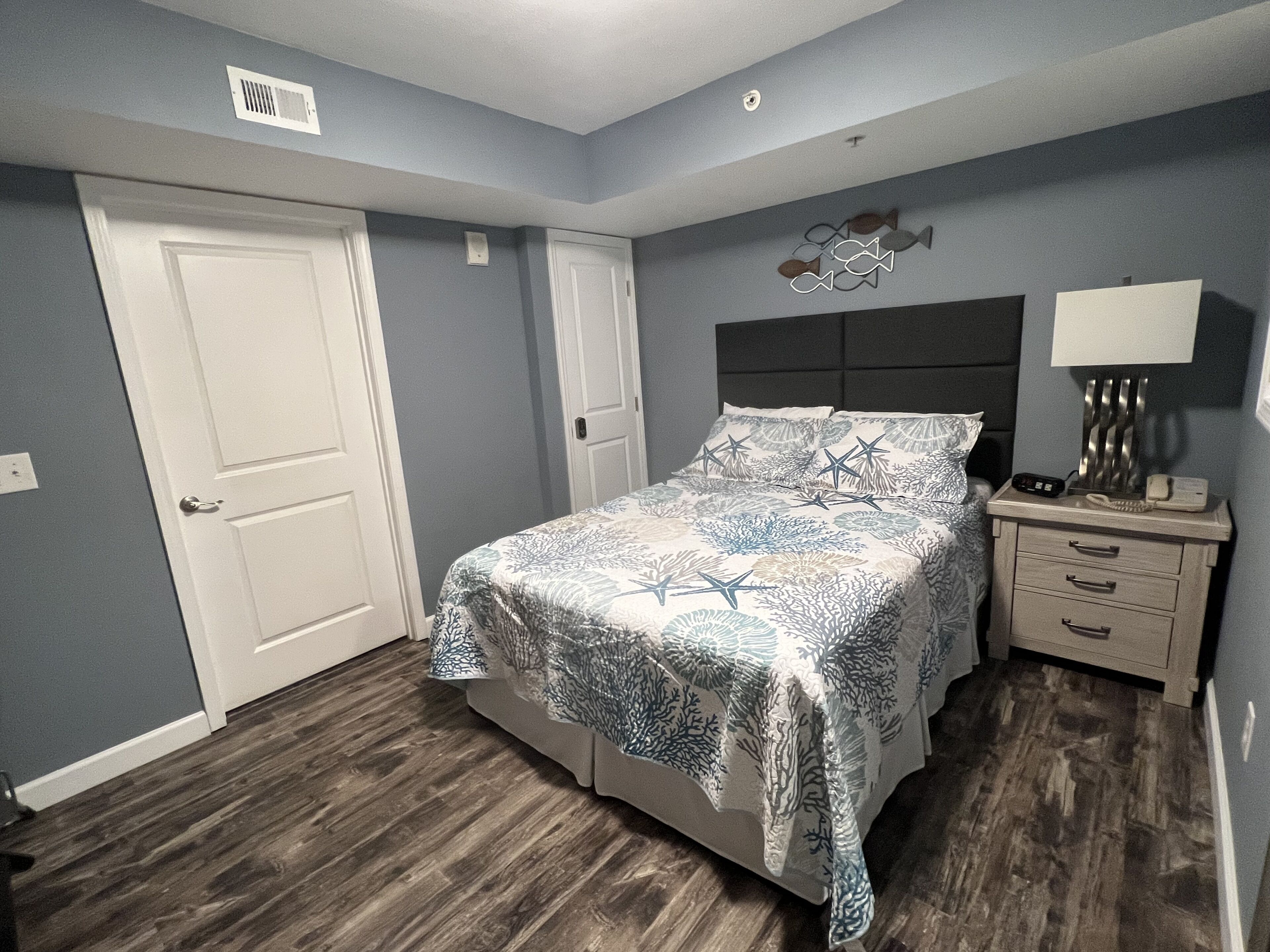 A bedroom with a bed, a nightstand, a lamp, and a wall decoration.