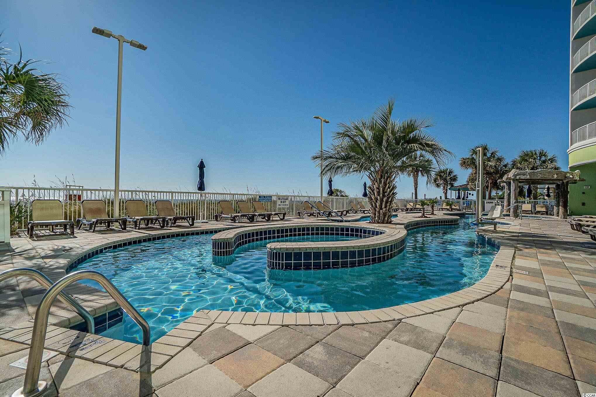 A swimming pool with a curved design, surrounded by lounge chairs and palm trees.