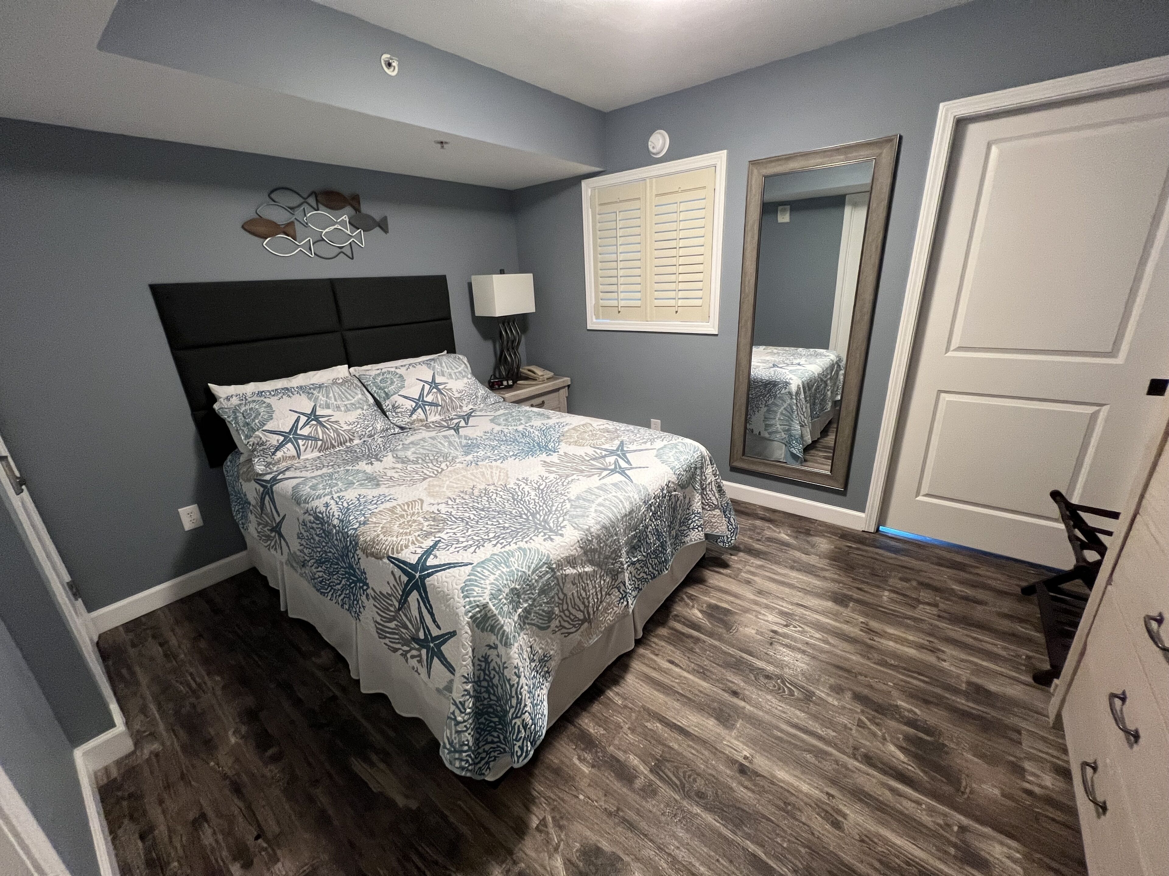 Un dormitorio con cama, mesita de noche, lámpara, decoración en la pared y una puerta.