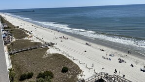 Une plage avec une promenade en bois qui mène à l’eau, une jetée visible au loin et des gens qui se détendent sur le sable.