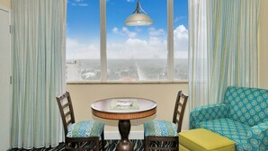 A room with a round table, two chairs, a sofa, and a view of a cityscape through a window with curtains. - Hollywood Beach Tower (Hollywood)