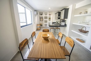 Une cuisine moderne avec des meubles blancs, une table à manger entourée de six chaises et une grande fenêtre qui laisse entrer la lumière naturelle.