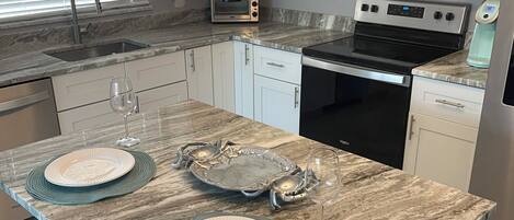 A kitchen with white cabinets, a built-in microwave, a stove, and a sink. There are two bar stools and a wine glass on the counter.