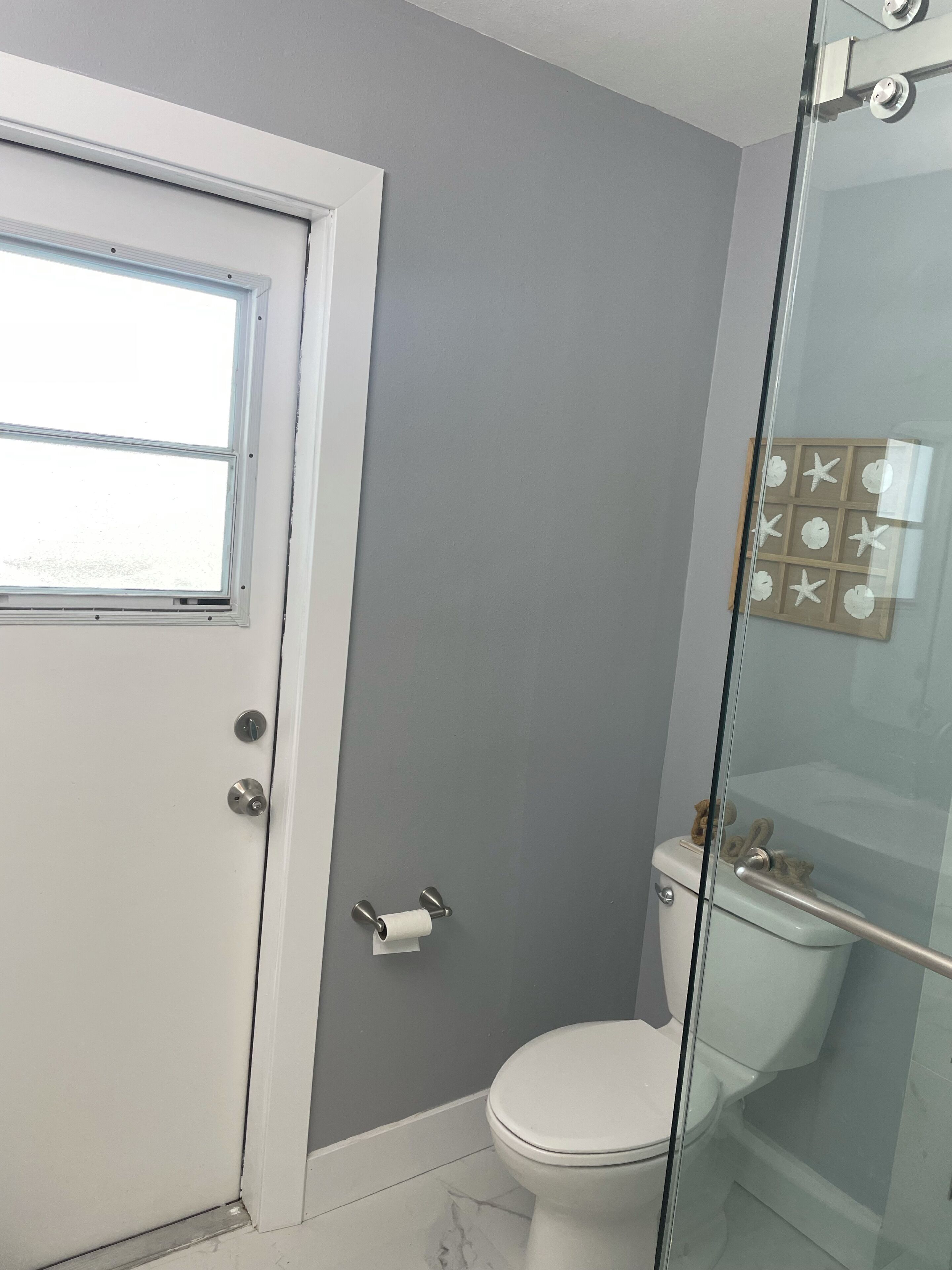Une salle de bain comprenant des toilettes, une douche à parois de verre et une porte avec une fenêtre.