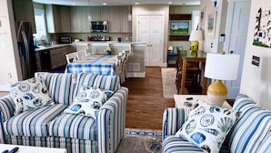 A modern living room with striped sofas, a dining area with a blue tablecloth, and a kitchen with stainless steel appliances. - 484 E Market - New construction close to town and the Beach! (Lewes)