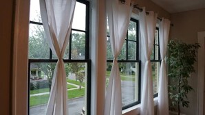 Habitació amb grans finestres, cortines blanques i una planta en test.