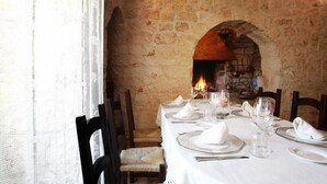 A dining table set for four with white tablecloths, plates, glasses, and napkins. An arched stone fireplace with a fire is visible in the background. - Tenuta Monacelle (Monopoli)