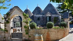 A stone building with a rounded entrance, a barrel, and a small garden with potted plants. - Tenuta Monacelle (Monopoli)