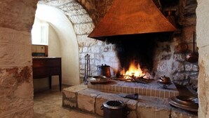 A stone fireplace with a large, ornate metal hood, a fire burning inside, and various pots and pans on the mantel. - Tenuta Monacelle (Monopoli)